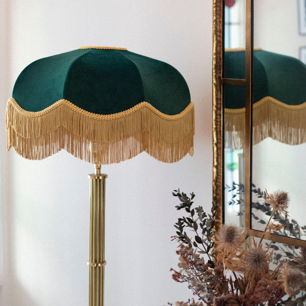 Decorative lamp with green shade and gold fringes against a white wall.