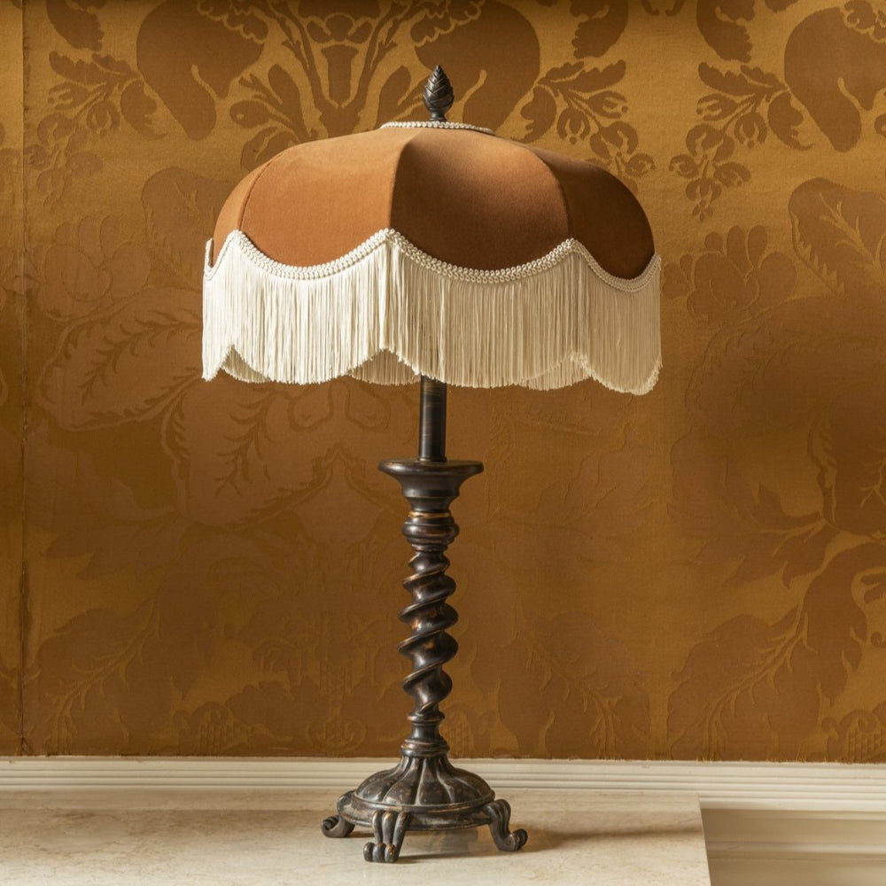 Decorative lamp with a brown shade and white fringe against a patterned wall.