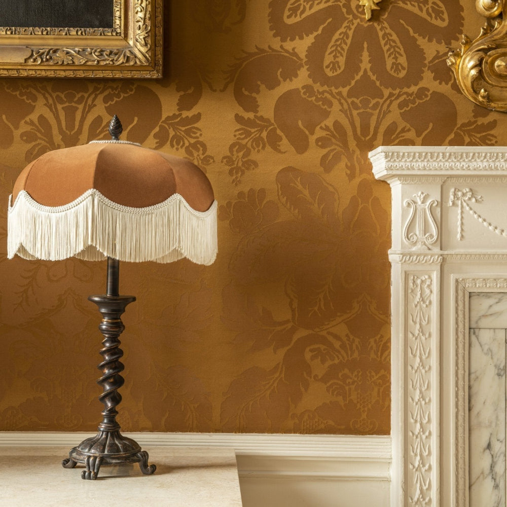 Decorative lamp with a fringed shade against a patterned wall.