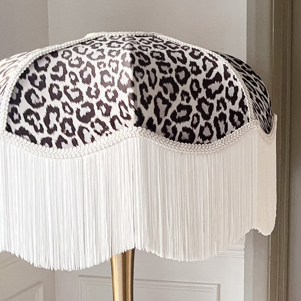 Lampshade with leopard print pattern and white fringe on a plain background