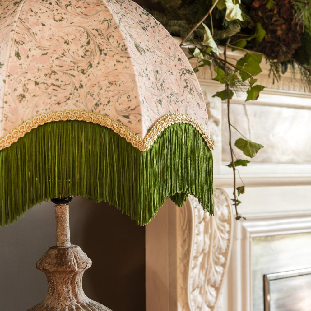 Decorative lamp with floral-patterned shade and green fringe against a neutral background