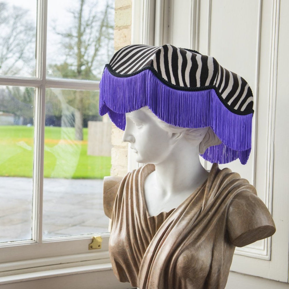 Mannequin head with a zebra-striped visor and purple fringe in front of a window.