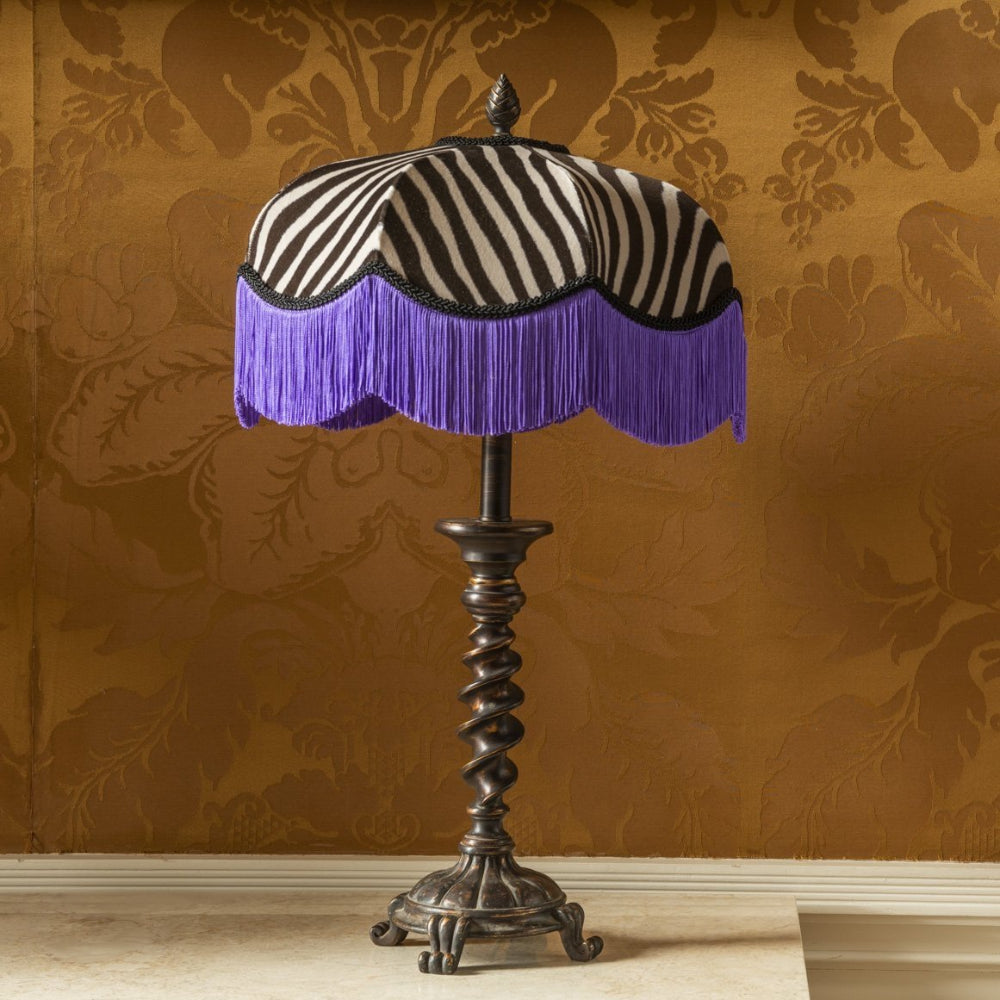 Decorative lamp with zebra print and purple fringe against a patterned wall.