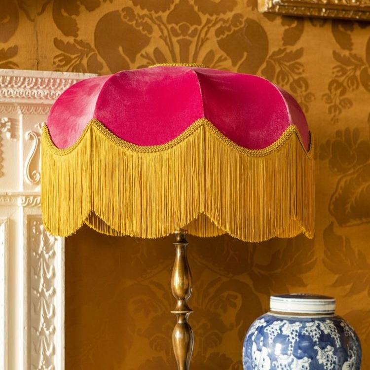 Pink lampshade with gold fringe on a decorative wall background