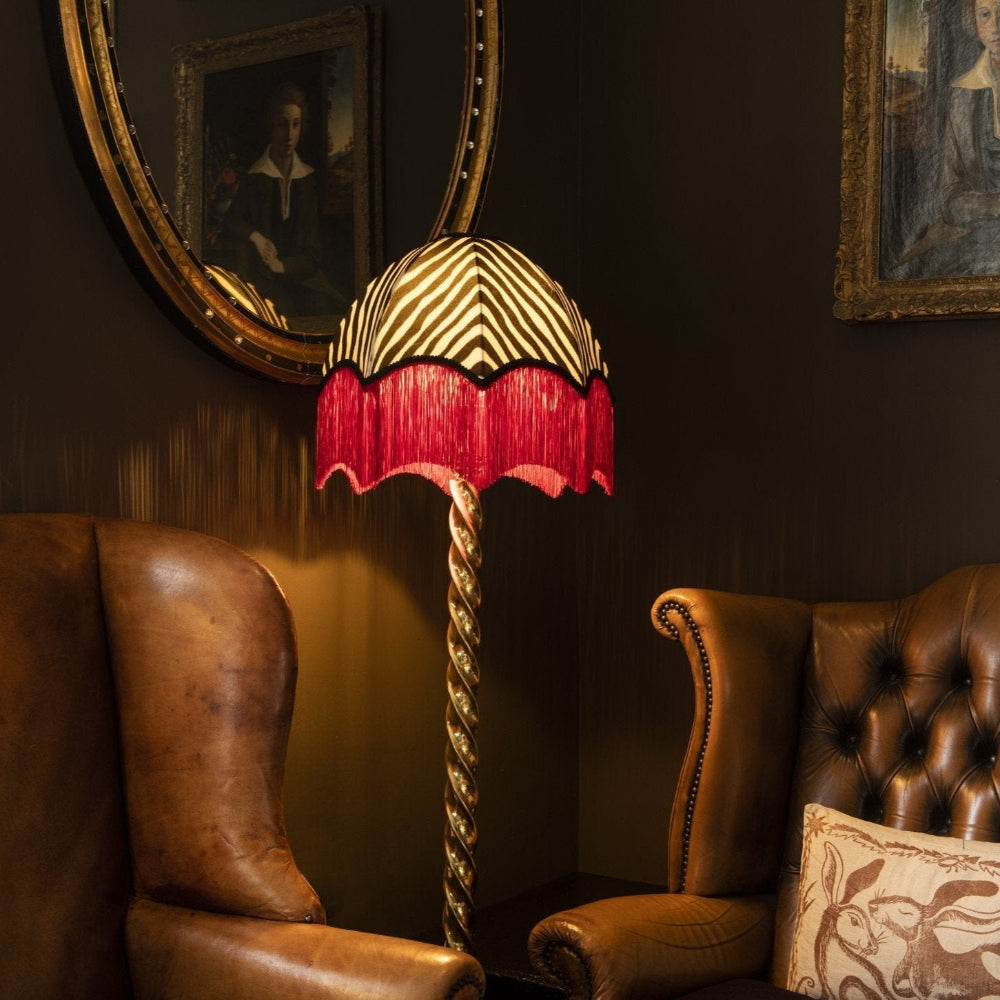 Decorative lamp with a red and gold shade in a room with brown leather chairs and framed pictures on the wall.