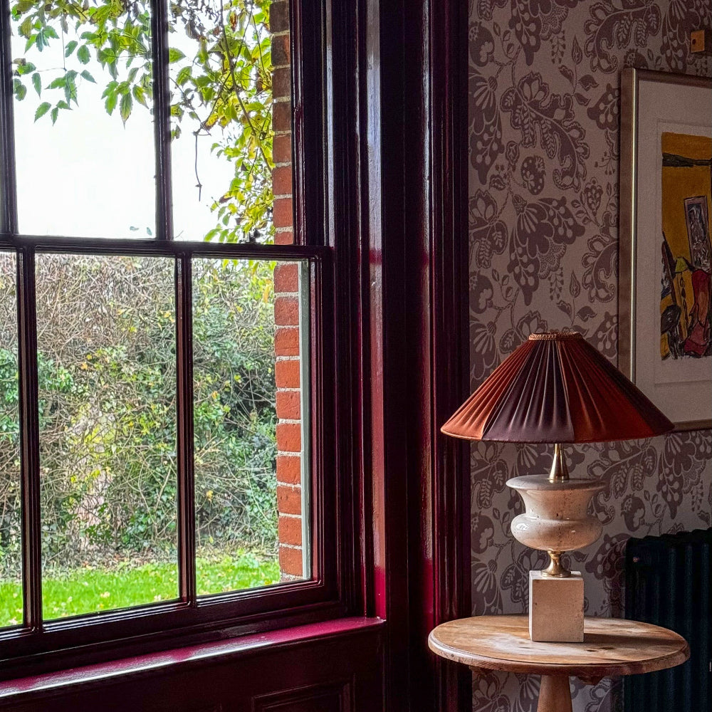 Lamp on a small table next to a window with a view of greenery