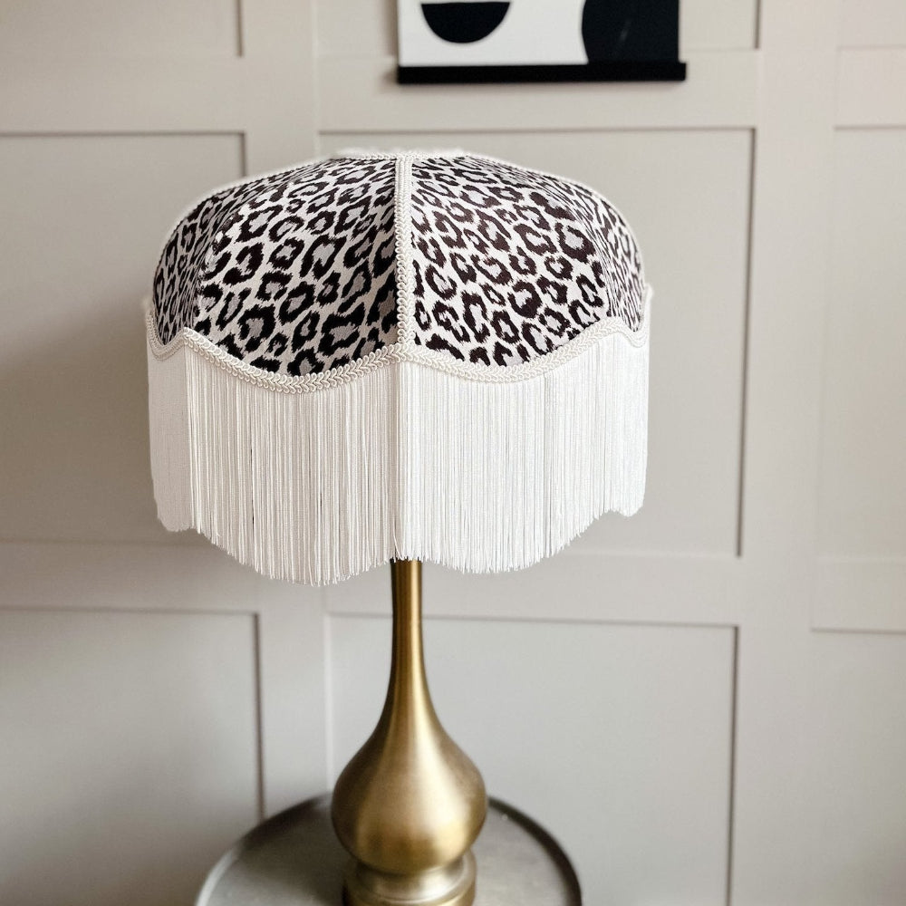 Table lamp with leopard print shade and gold base against a white paneled wall.