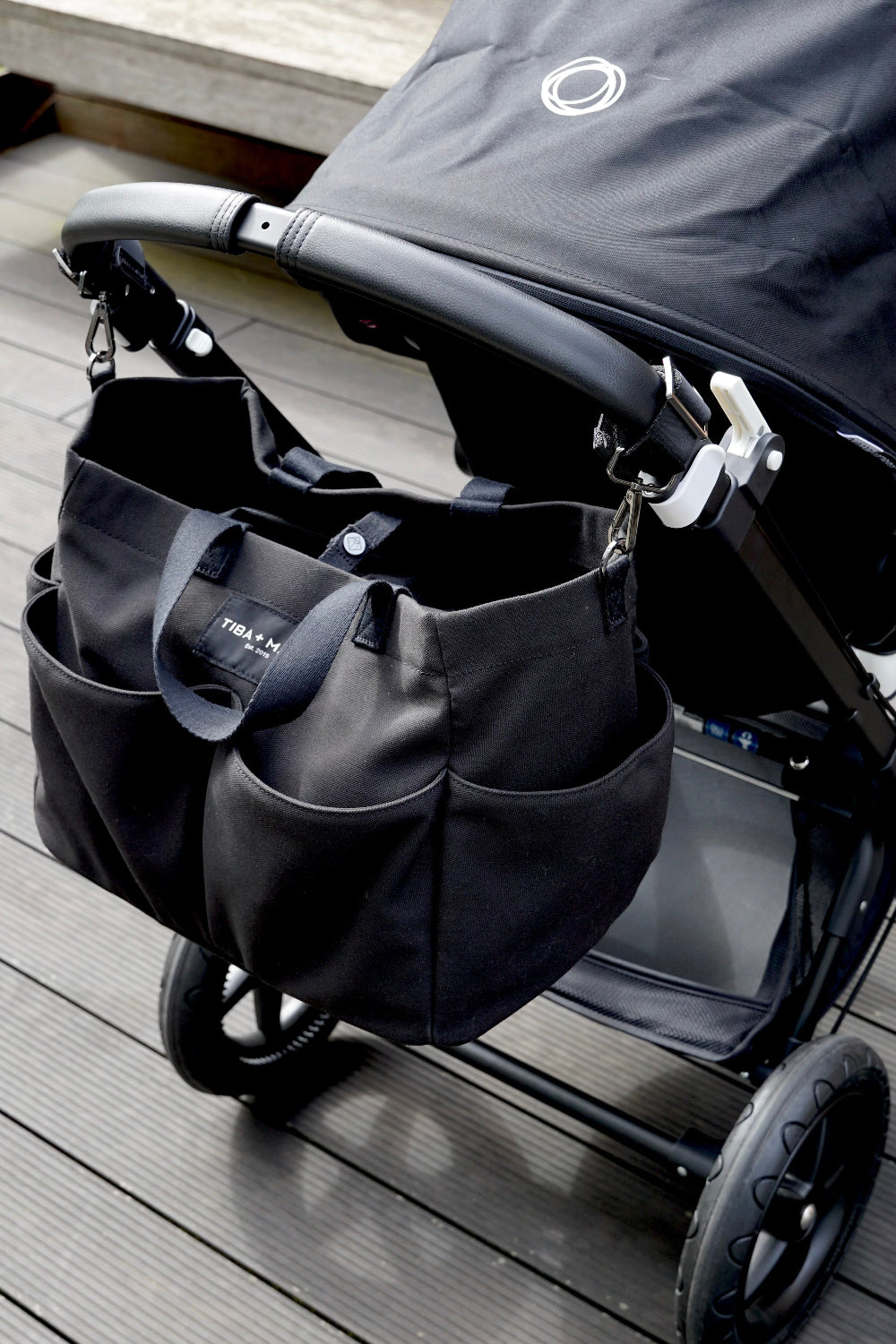 Black stroller with attached black bag on decking outside.