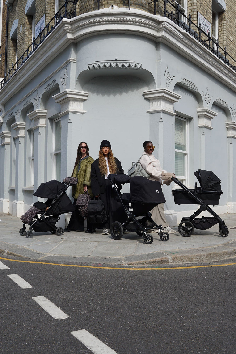 Three women with strollers standing on a street corner in an urban setting.