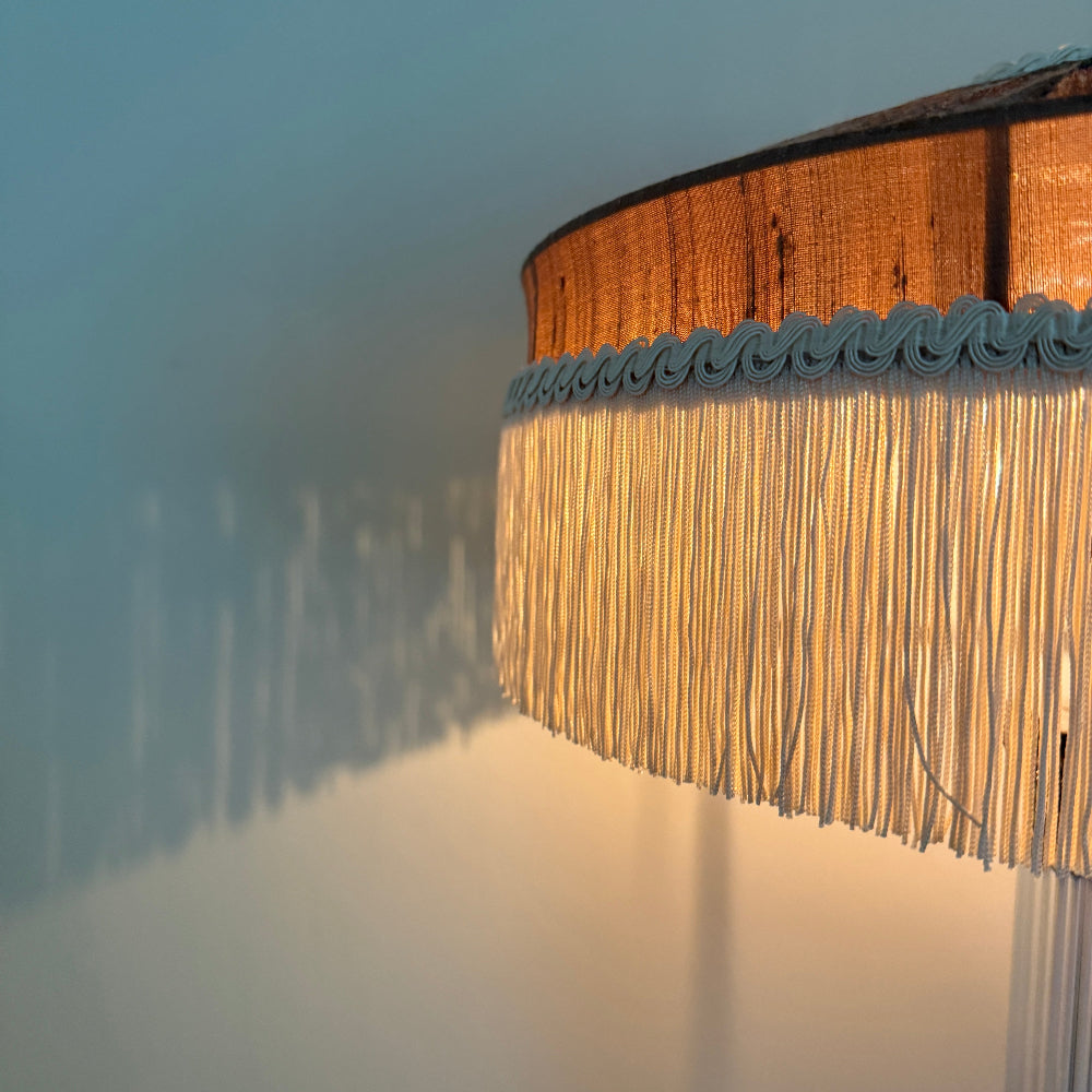 Woven lampshade with fringe detail on a soft focus background