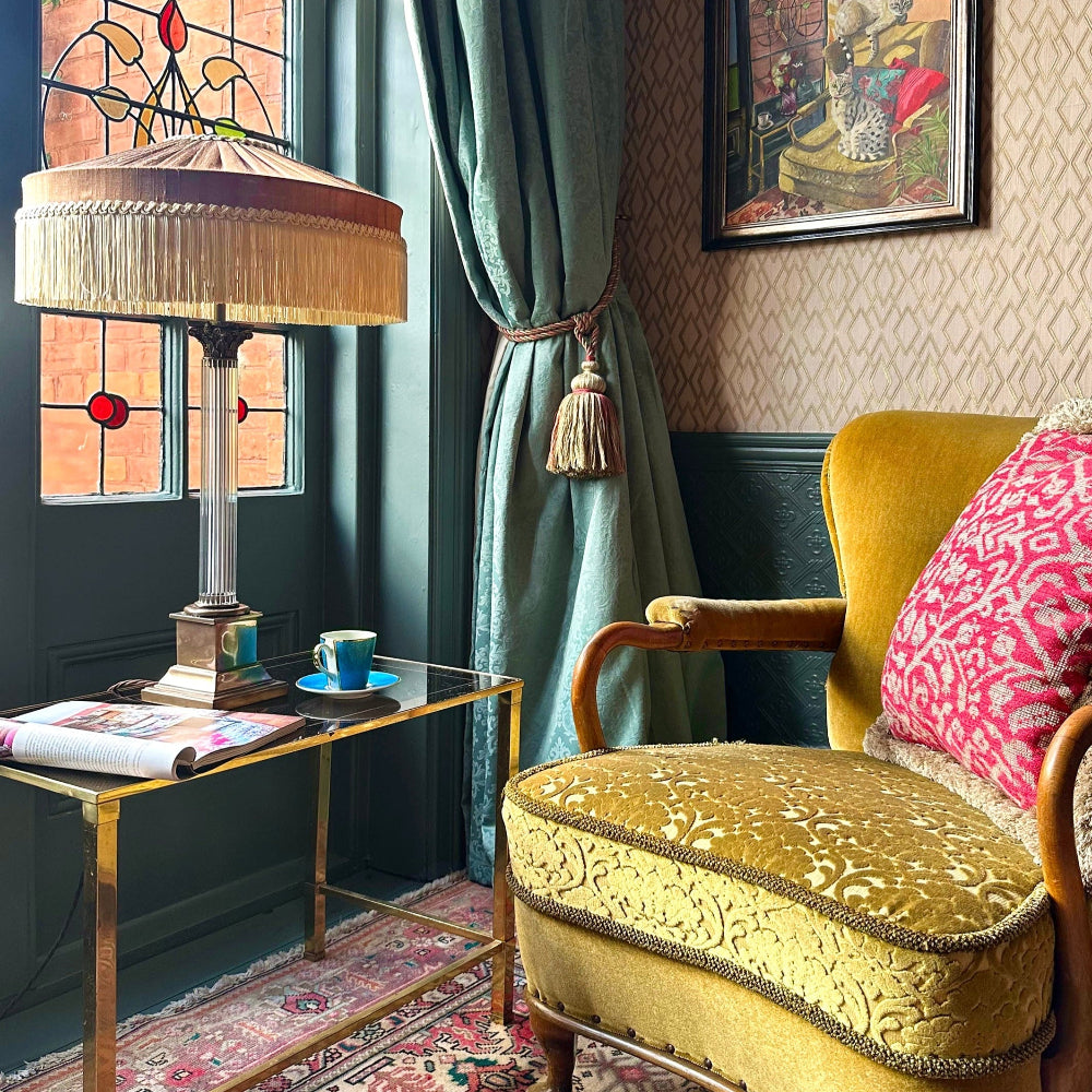 Decorative interior with a yellow armchair, Peggy Silk Fringed lampshade, and stained glass window.