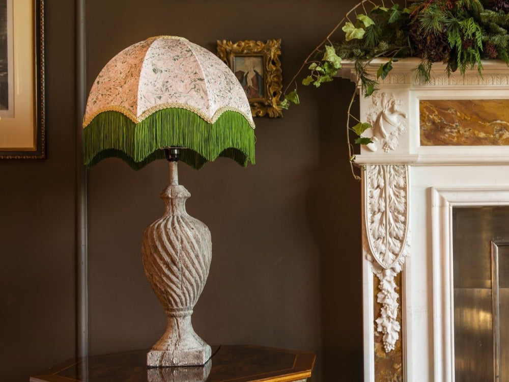 Decorative lamp with a striped green and white shade on a wooden surface next to a fireplace.