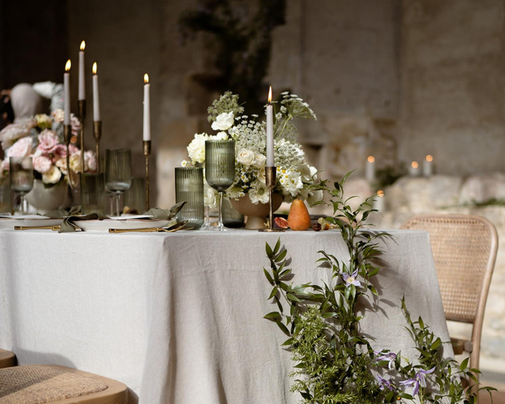 Elegant table setting with floral arrangements, candles, and greenery in a softly lit room.
