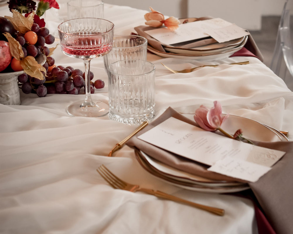 Elegant table setting with wine glasses, plates, and cutlery on a white tablecloth.