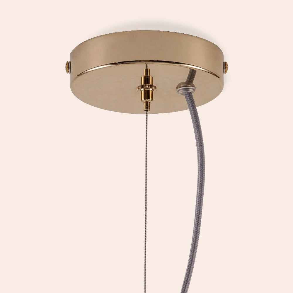 Ceiling light fixture with gold finish and gray cord on a beige background