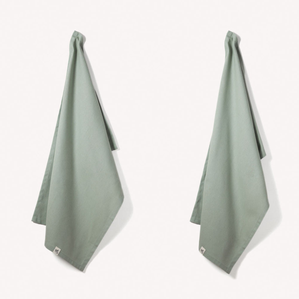 Two green towels hanging on a white background