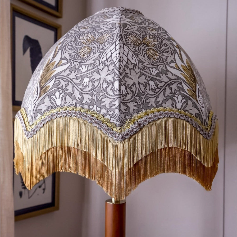 Decorative lamp with intricate William Morris design and gold fringe against a neutral background