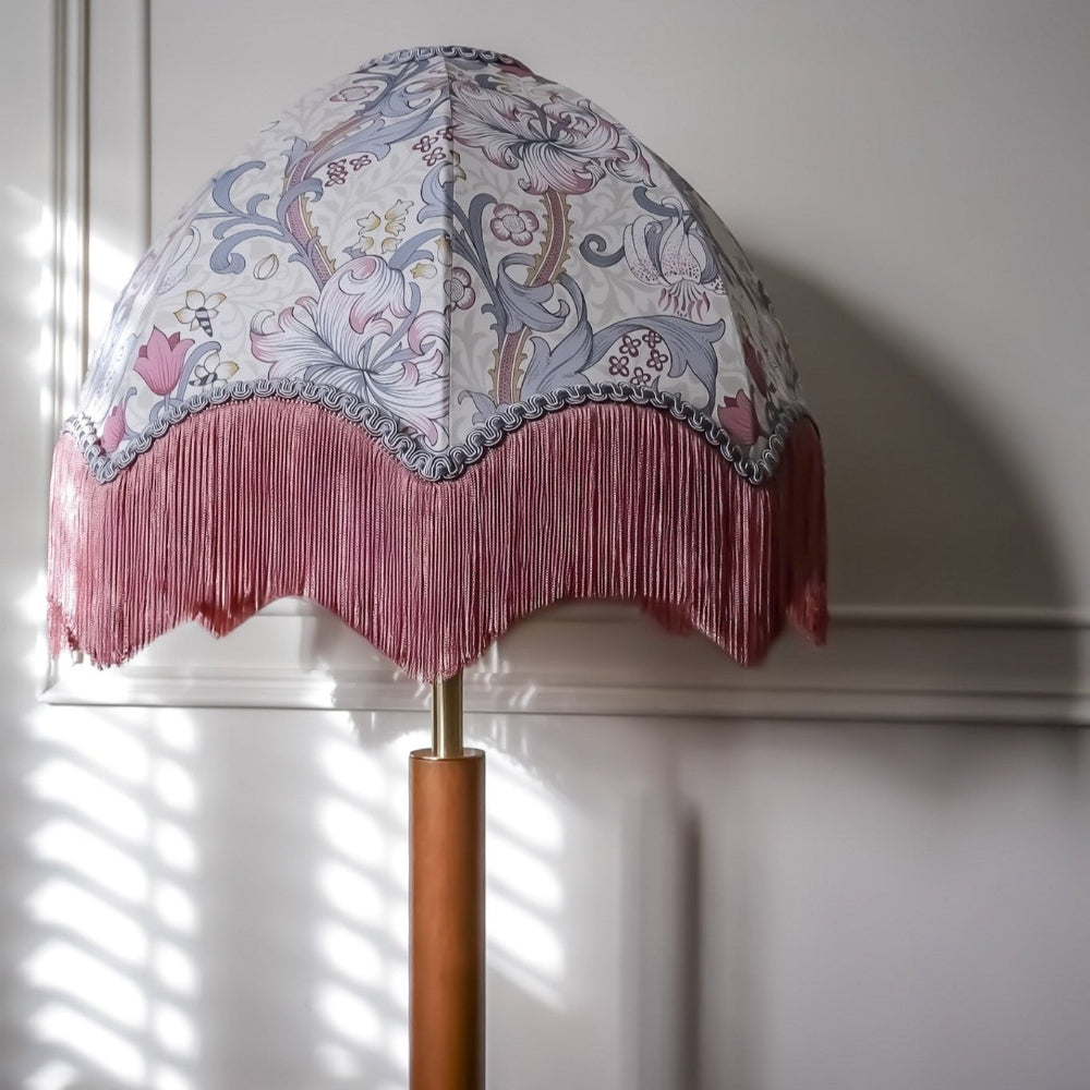 Decorative lamp with floral patterned shade and pink fringe against a white wall.