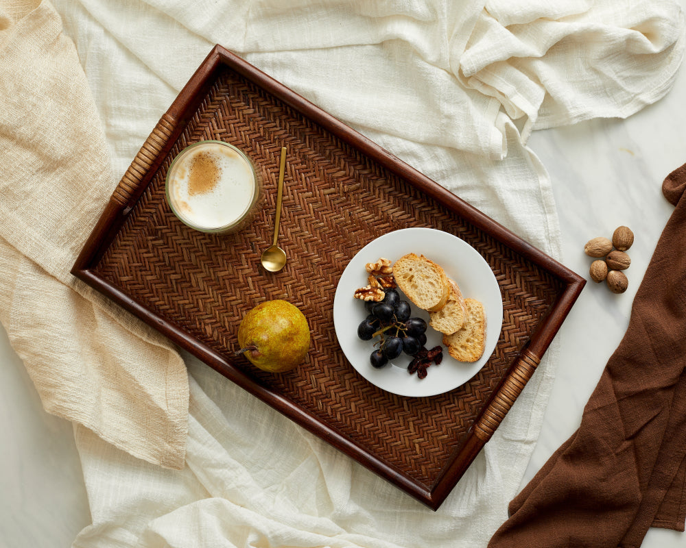 Wooden tray with a cup of coffee, plate of snacks, and fruit on a white fabric background