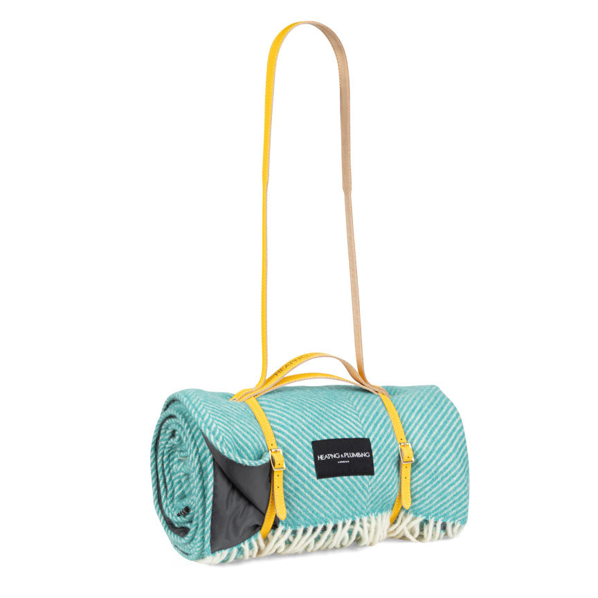 Roll-up teal picnic mat with yellow strap on a white background