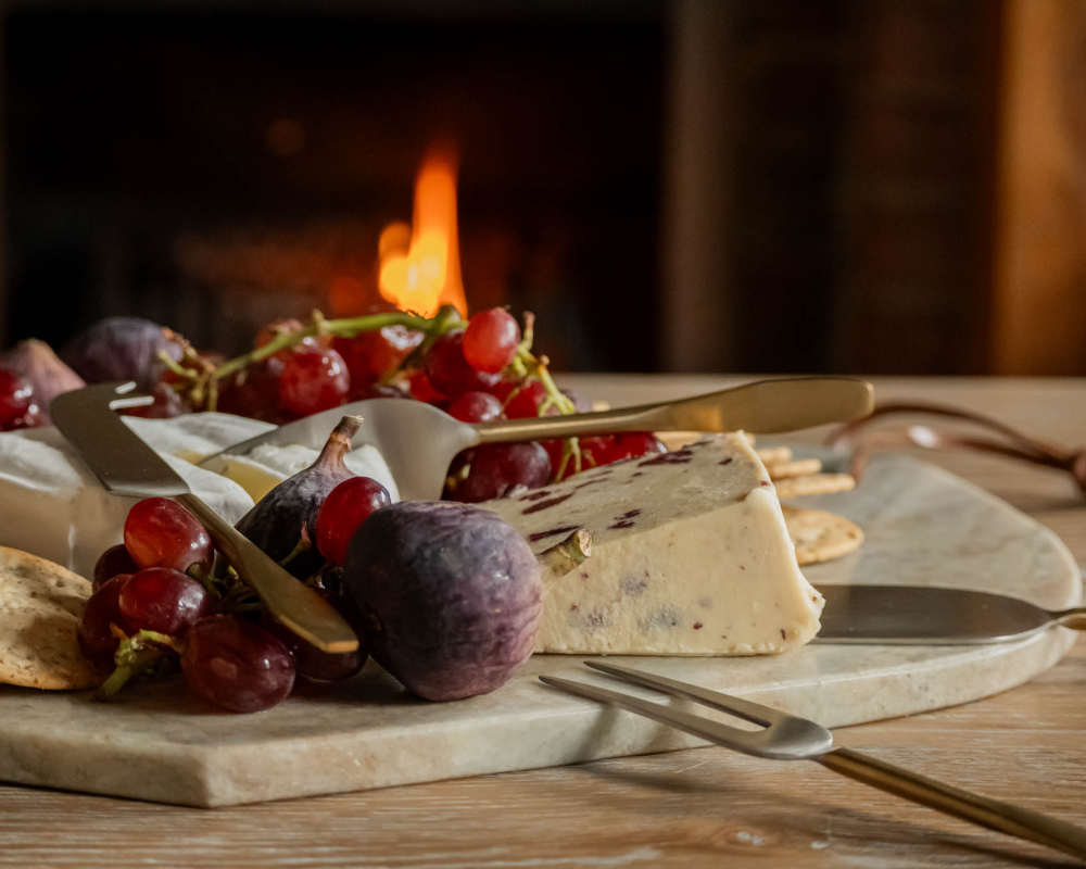 Platter of cheese, grapes, and figs with a fireplace in the background
