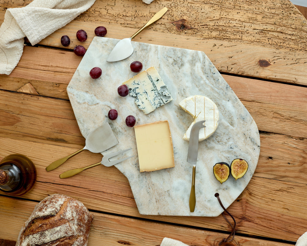 Marble cheeseboard with assorted cheeses, figs, and bread on a wooden table.