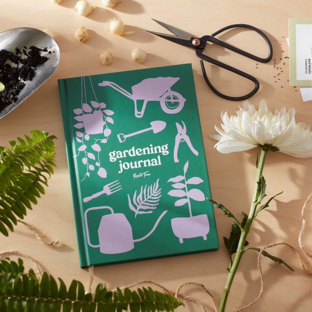 Gardening journal with gardening-themed illustrations on a table with plants and tools.