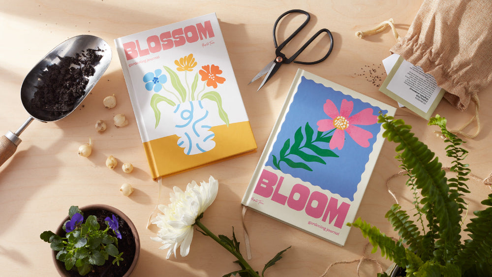 Two books titled 'Blossom' and 'Bloom' on a table with gardening tools and plants.