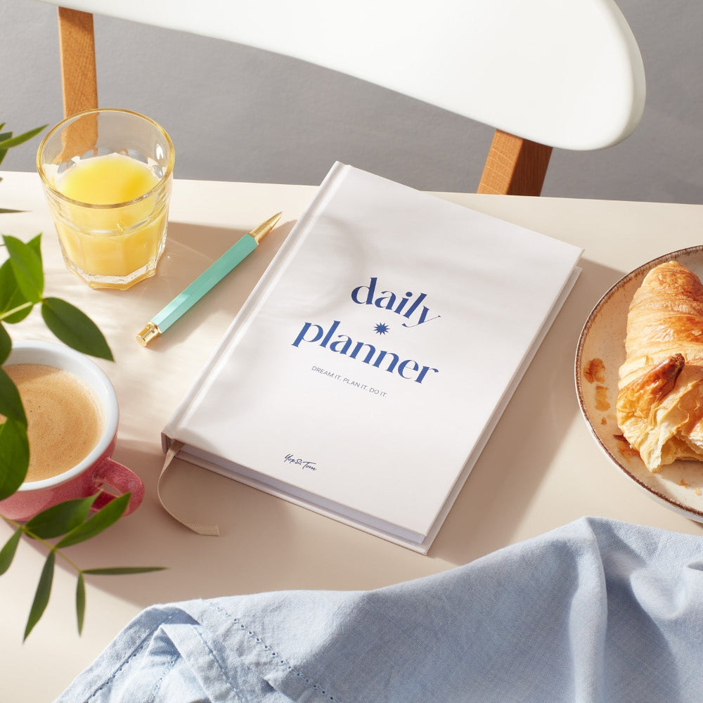 Daily planner book on a table with a glass of orange juice, cup of coffee, and croissant.