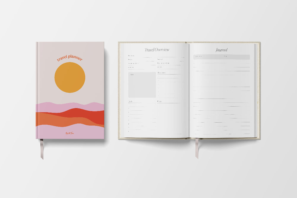 Journal with a colourful cover featuring a sun and mountains, open to a blank page on a white background.