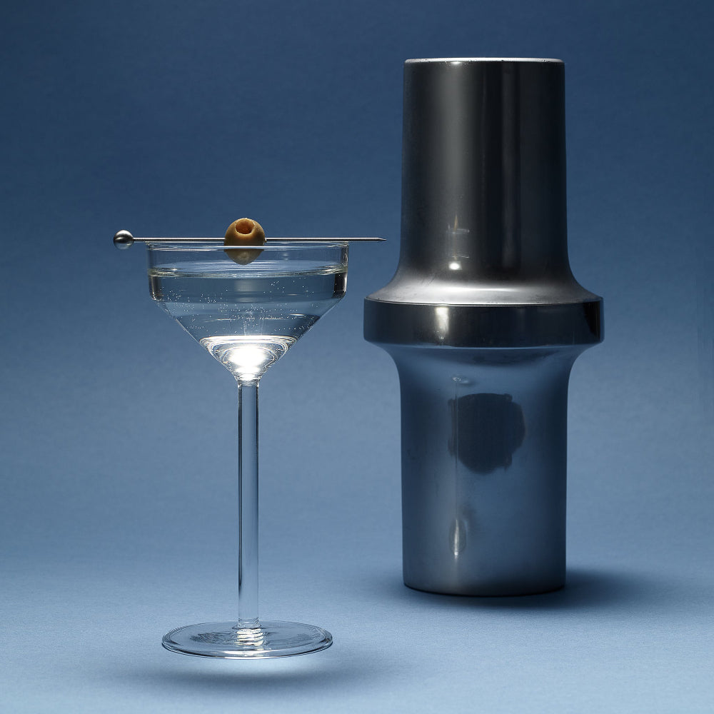Aaron Probyn BARBICAN brushed stainless steel cocktail shaker beside a Martini glass on a blue surface