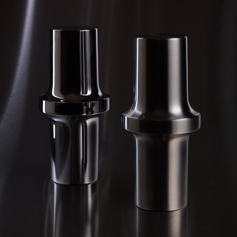 Two Aaron Probyn BARBICAN cocktail shakers in brushed and polished stainless steel on a dark reflective surface