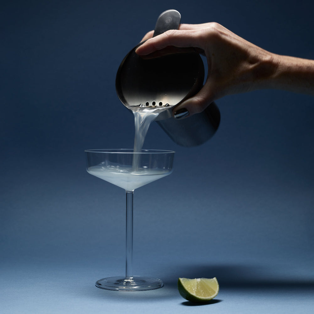Cocktail being poured through the Aaron Probyn BARBICAN stainless steel strainer into a stemmed coupe glass