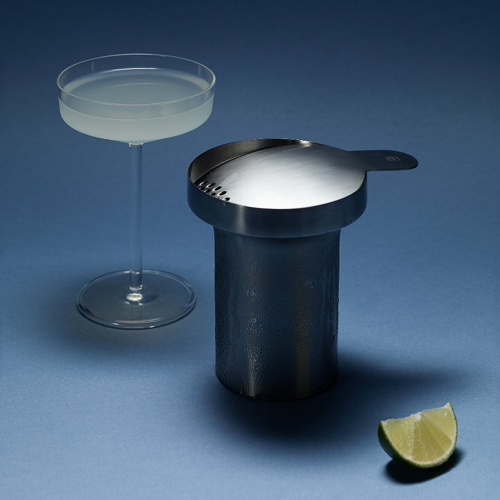 Aaron Probyn BARBICAN stainless steel cocktail strainer resting on a shaker beside a coupe glass and lime wedge