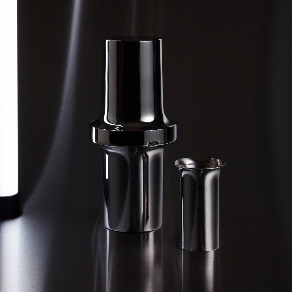 BARBICAN stainless steel cocktail jigger beside the matching shaker on a dark reflective surface
