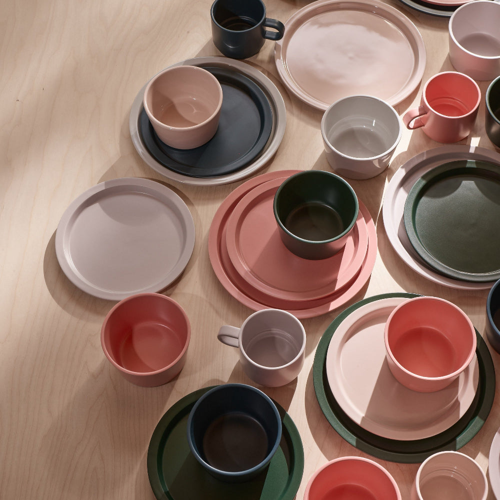 A collection of pastel-colored ceramic tableware, including plates, bowls, and mugs, arranged in a flat-lay pattern on a light wood floor.