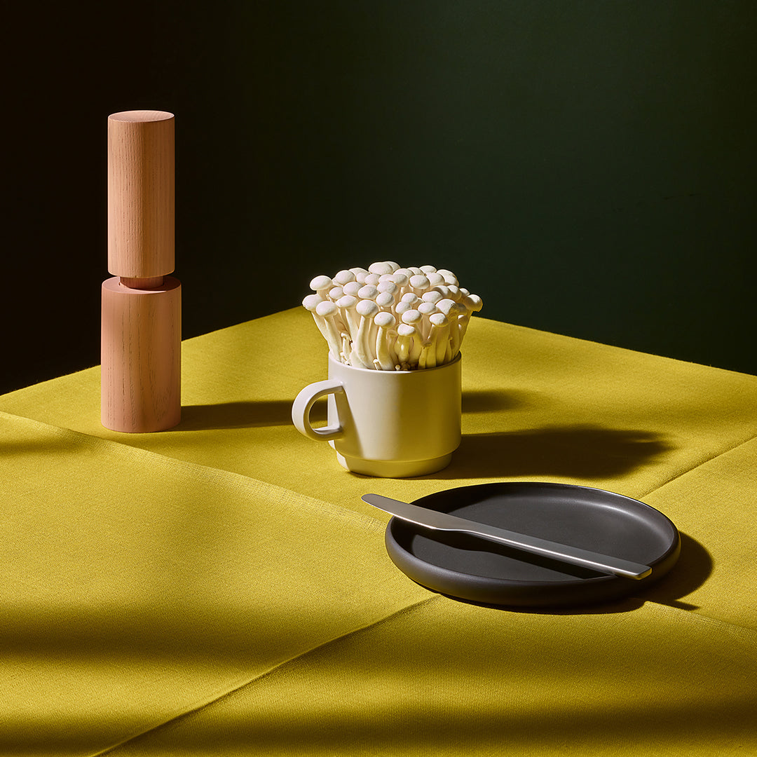 Ceramic mug with white ceramic mushrooms on a yellow fabric surface with a dark background