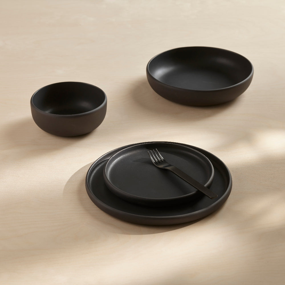 Black COLOMBO porcelain serving bowl by Aaron Probyn displayed with matching black bowls and plates