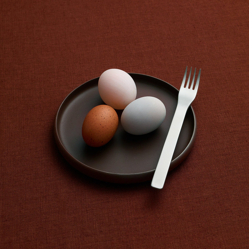 Black COLOMBO porcelain side plate by Aaron Probyn holding three eggs with a silver fork