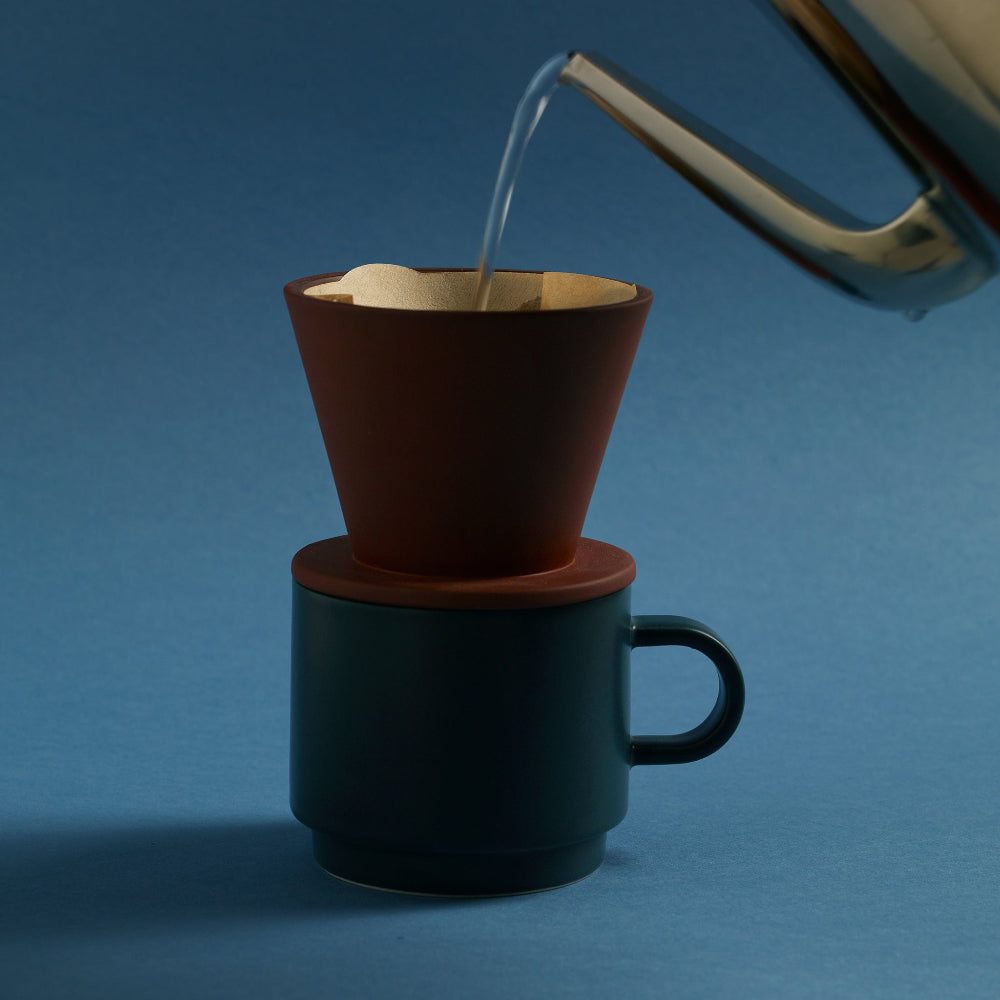 Hot water being poured into an Aaron Probyn COLOMBO terracotta coffee dripper on a dark teal mug