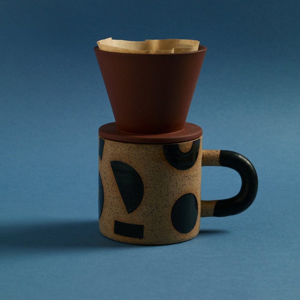 Aaron Probyn terracotta coffee dripper on a beige ceramic mug with bold black abstract shapes