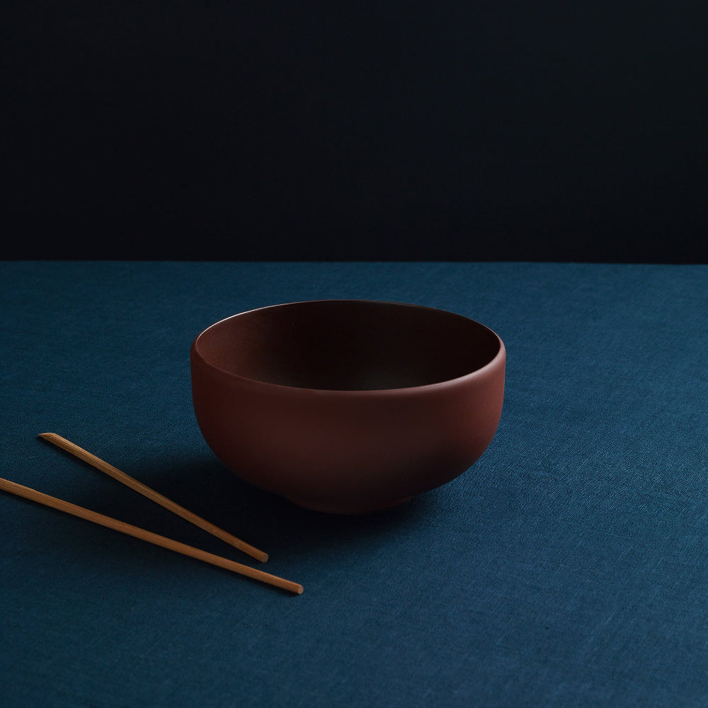 Empty terracotta porcelain ramen bowl with wooden chopsticks on a blue surface