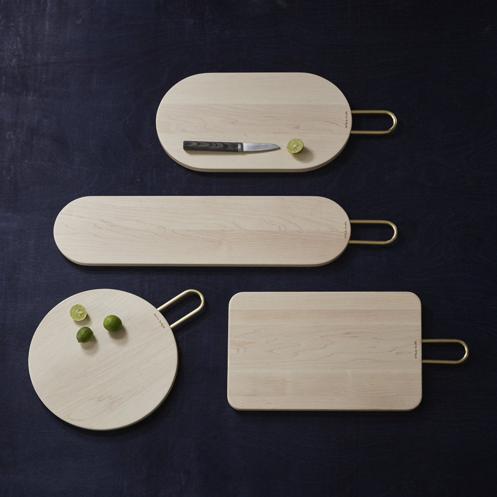 Four Aaron Probyn HEATH maple wood chopping and serving boards with brass handles on a dark background