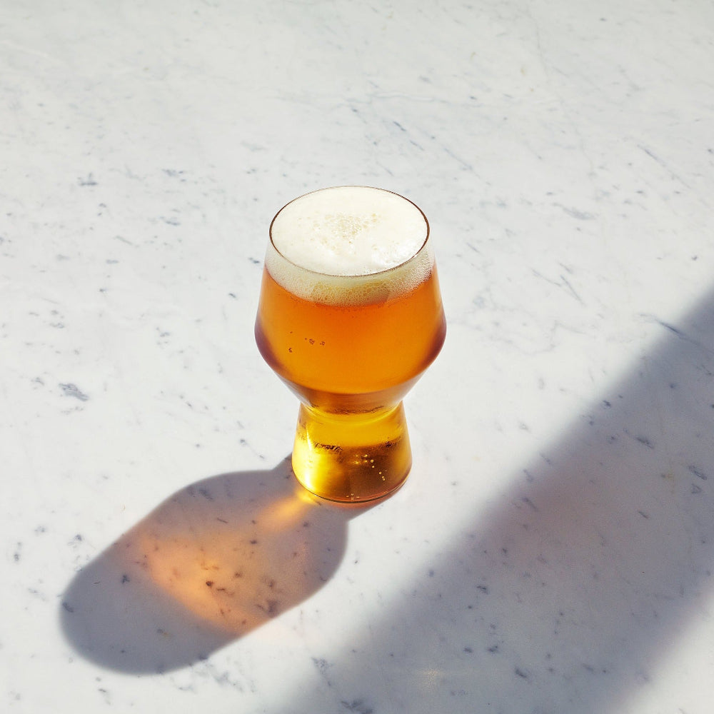 Aaron Probyn JUNIPER geometric beer glass filled with golden beer on a marble surface, viewed from above