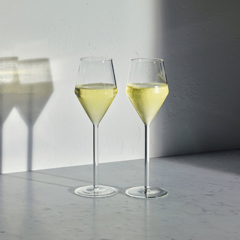Two Aaron Probyn JUNIPER Champagne tulip glasses filled with sparkling wine on a marble surface