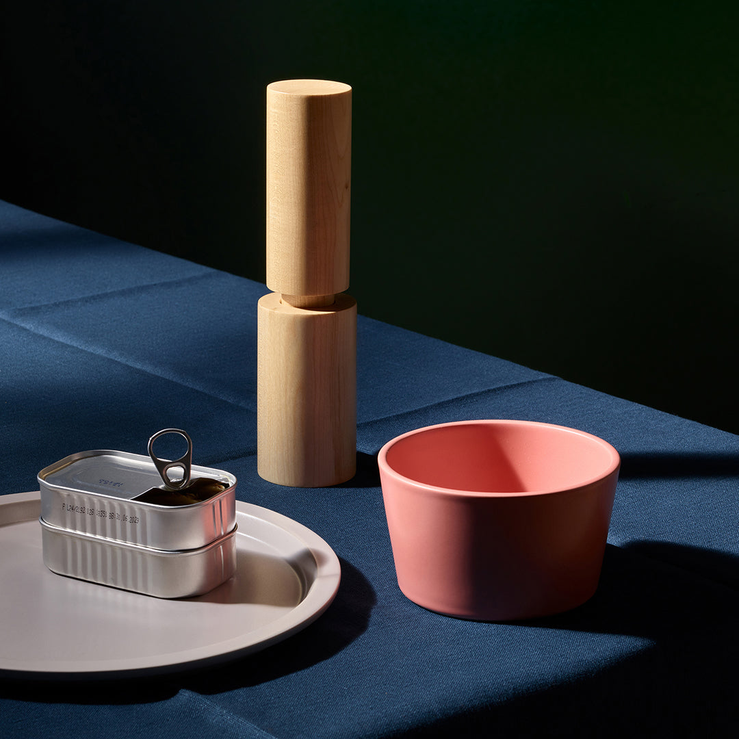 Wooden salt grinder, pink bowl, and metal container on a blue surface with a dark background