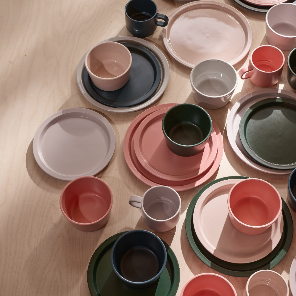 A styled flat-lay collection of pastel-colored ceramic tableware, including plates, cups, and mugs, arranged on a light wood surface.