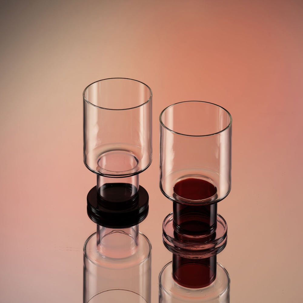 Two clear wine glasses with dark bases, set against a warm peach gradient background.