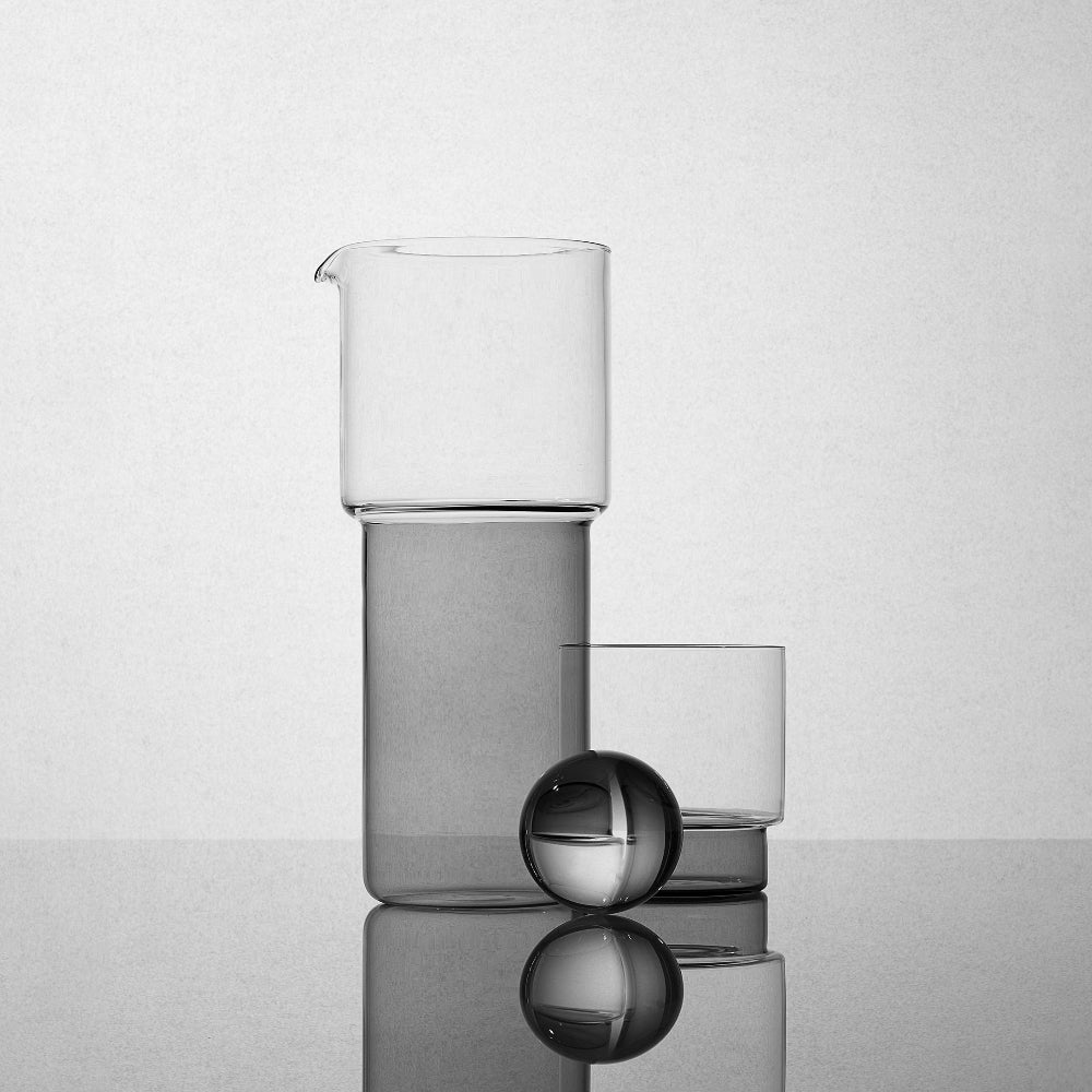 Set of glass tumblers on a reflective surface with a light gray background