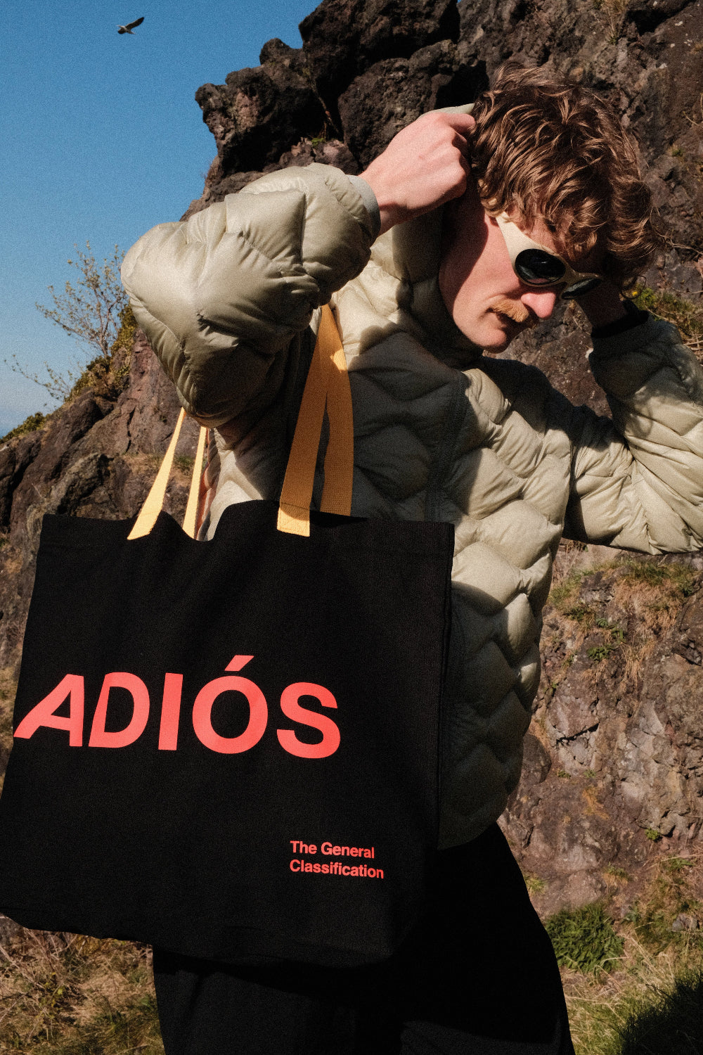 Person holding a black bag with 'ADIÓS' text against a rocky background